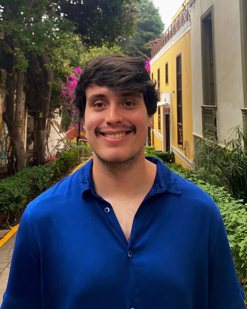 Gabriel Marinho, psicólogo clínico, sorrindo, de camisa azul, em uma rua arborizada